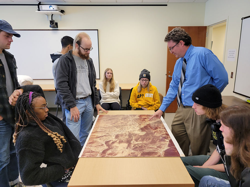 Students and faculty look at an aerial photograph of campus.