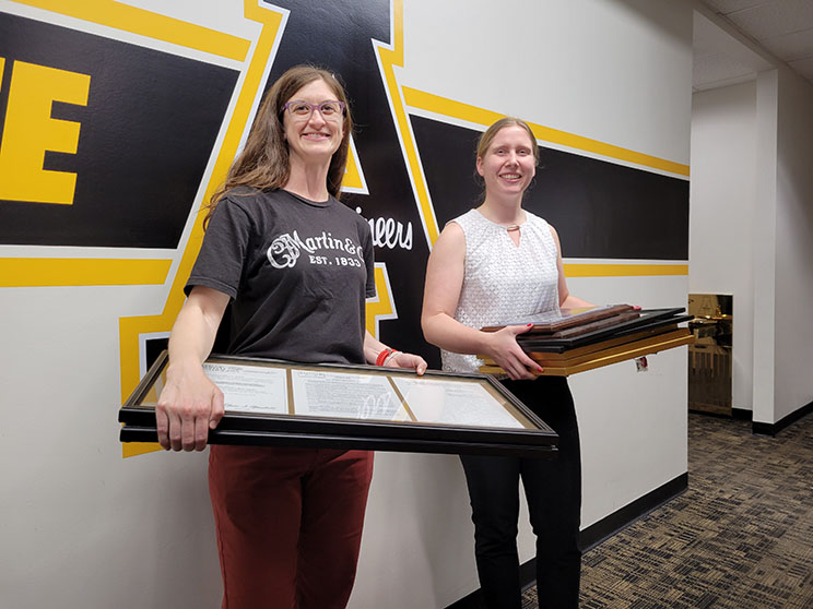 Anna Smith and Crista Bain holding framed items donated to the University Archives.