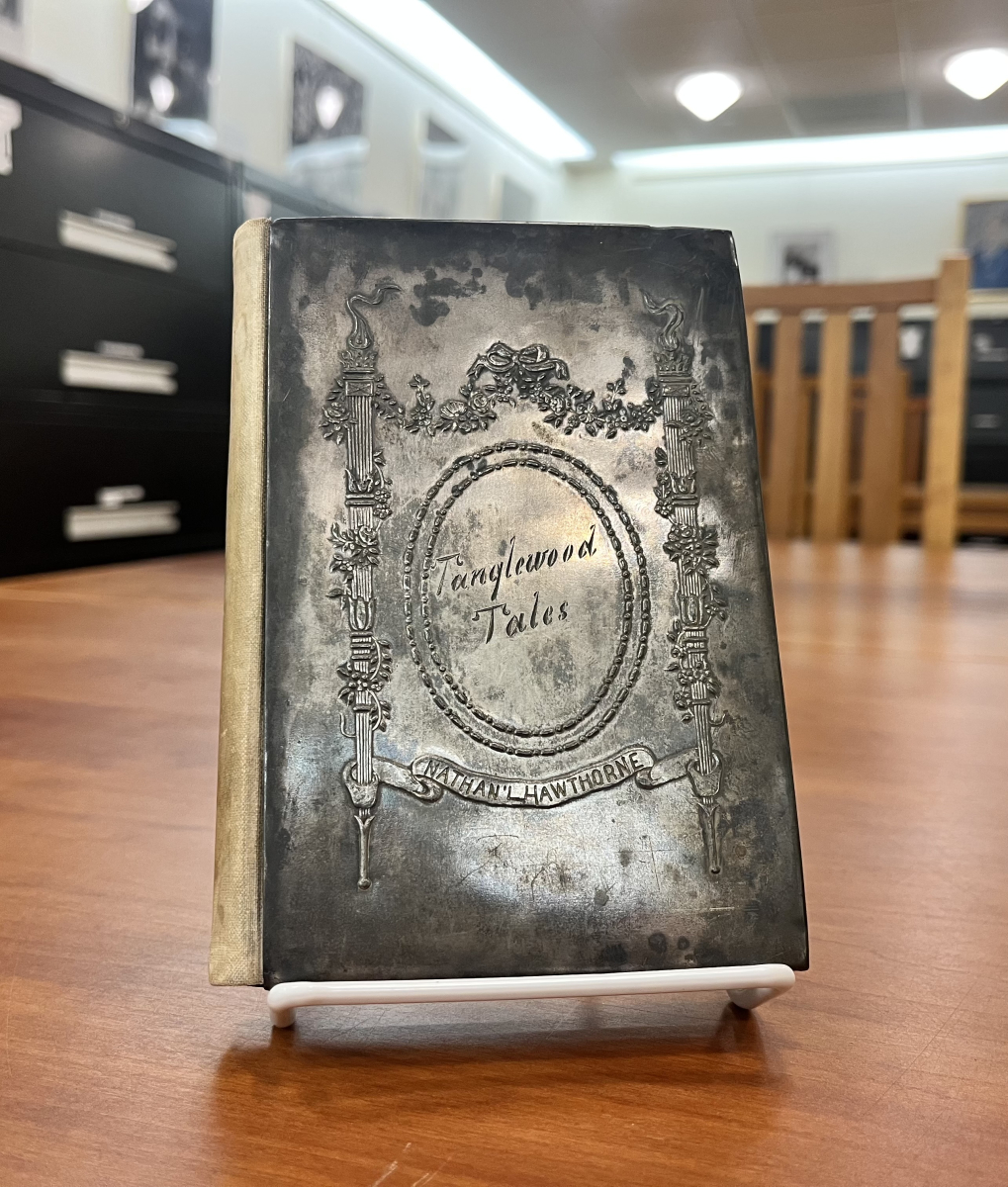An antique book titled "Tanglewood Tales" by Nathaniel Hawthorne. The front cover features a tarnished, metallic silver plate embossed with neoclassical pillars, floral garlands, and an oval border surrounding the cursive title "Tanglewood Tales." A banner below reads "Nathan'l Hawthorne."