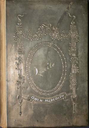 Close-up of the front cover of an antique book, showing a heavily tarnished metal book cover. The design features a decorative neoclassical framework with columns and floral garlands framing a central beaded oval. Inside the oval, the title "Lucile" is embossed, and a ribbon banner below reads "Owen Meredith."