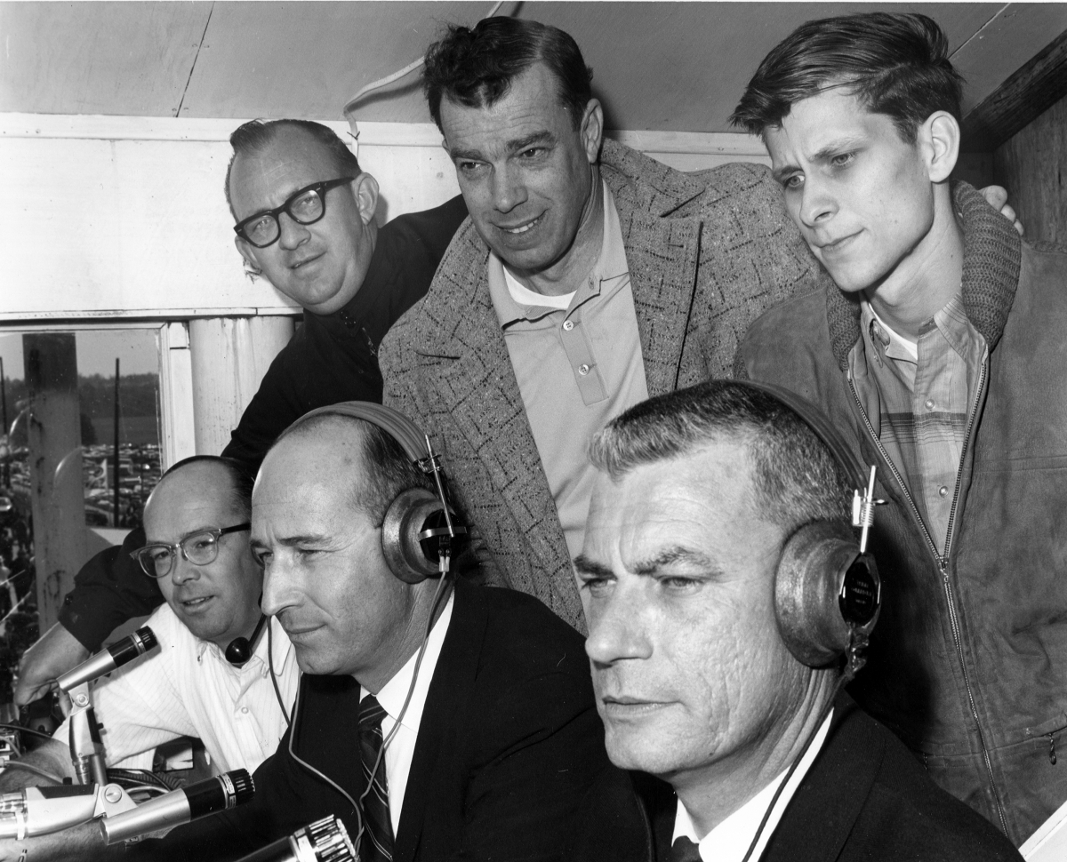 Hank Schoolfield (seated, center) announces a race on the Universal Racing Network. Jerry Perryman is on the left and Bob Montgomery on the right. Standing behind Perryman is Hal Hamrick.