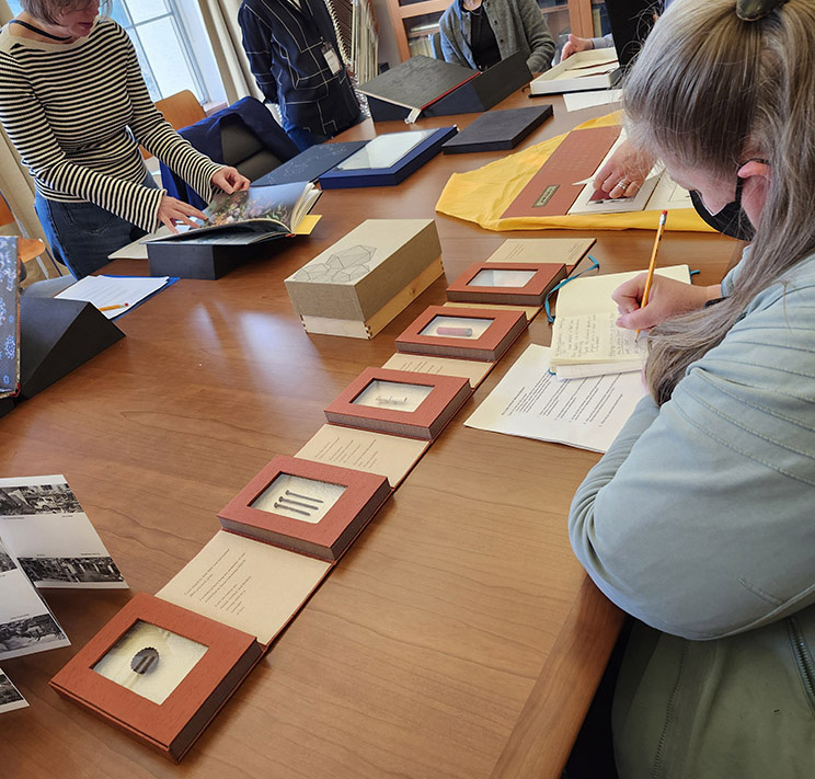 Seminar students looking at and taking notes on books at a large table.
