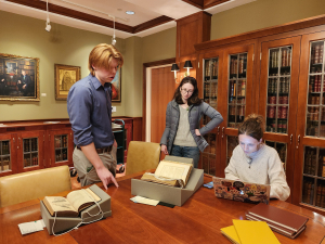 Three people examining a book in a rare book library.