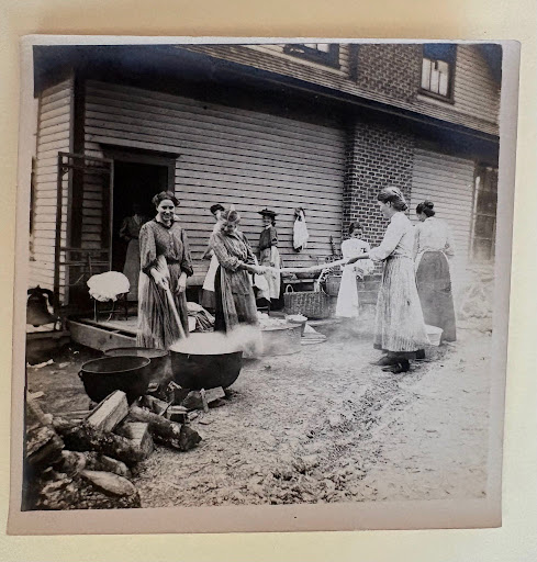 Women gathered outside with wash pots and firewood, possibly preparing laundry.